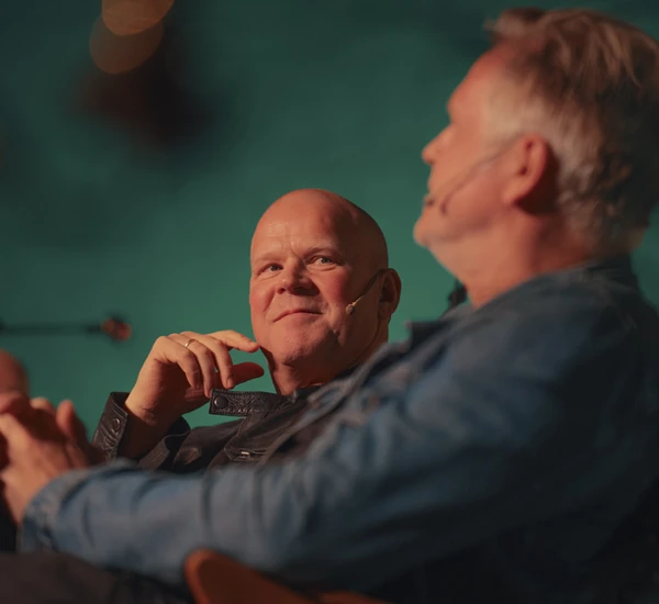Skuespillerne Anders Baasmo og Trond Espen Seim sitter på en scene og snakker sammen. Nærbilde, froskeperspektiv. Foto.